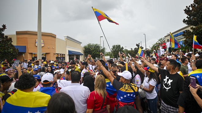 A crowd packs together on an Orlando street, waving Venezuelan flags