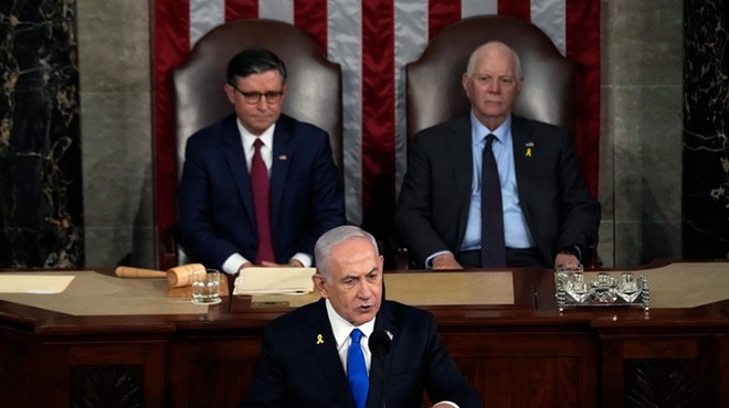 netanyahu at the dais with Speaker of the House Mike Johnson (R-LA) and U.S. Sen. Ben Cardin (D-MD) seated in the background, flanking him and slightly out of focus