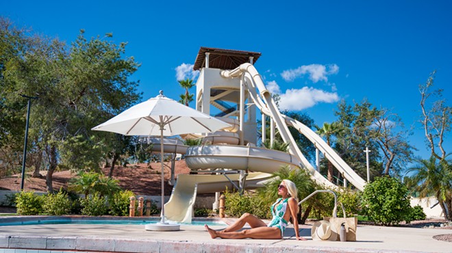 A woman sitting by a pool with a waterslide in the background.