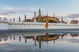 A photograph of a monk walking in the morning after the rain in front of the Temple of the Emerald Buddha (Wat Phra Kaew), part of the Grand Palace, in Bangkok, Thailand