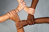 A photograph of many hands, each with a different skin color, holding each other together