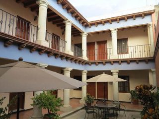 Two-story courtyard with columns, balconies, and outdoor seating. Brown doors on upper level, with large umbrellas and potted plants on the ground level.