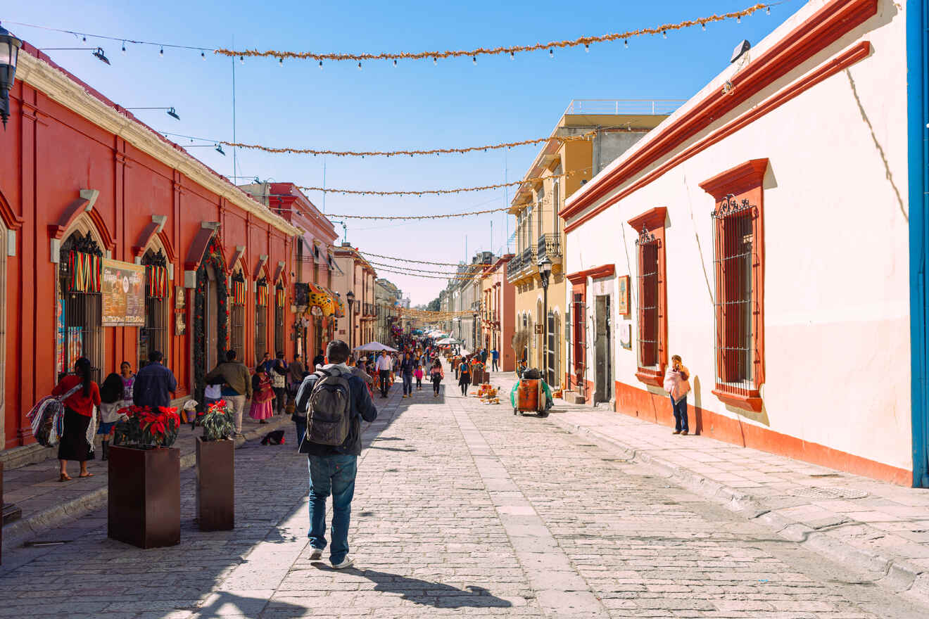 A bustling street scene with people walking along a cobblestone path lined with colorful buildings and festive decorations overhead.