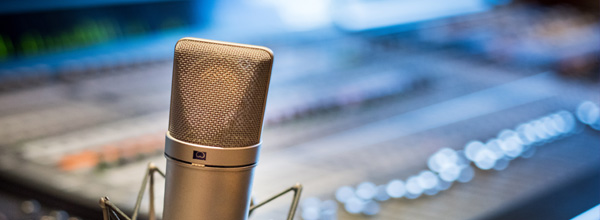 A microphone sits in focus in front of a multi-channel audio control board