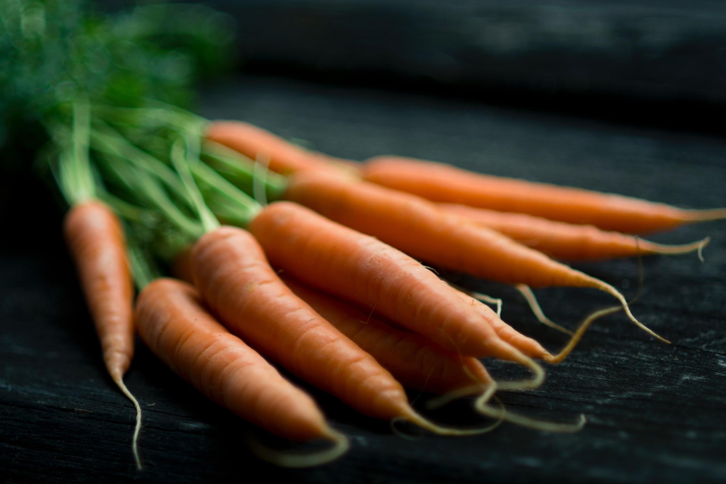 A bunch of orange carrots are shown laying on a dark table