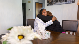 Two women hug at a table.