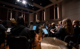 A professor conducts a mixed chamber ensemble onstage.