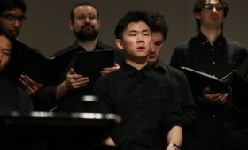 Singers hold choir books and perform onstage.