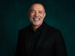 Photo of composer Michael Abels in front of a dark green canvas background.