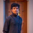 Choral student in layers of concret black attire poses in front of an ornate doorway.