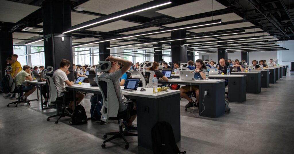 Group of people working on their laptops in a large work space.