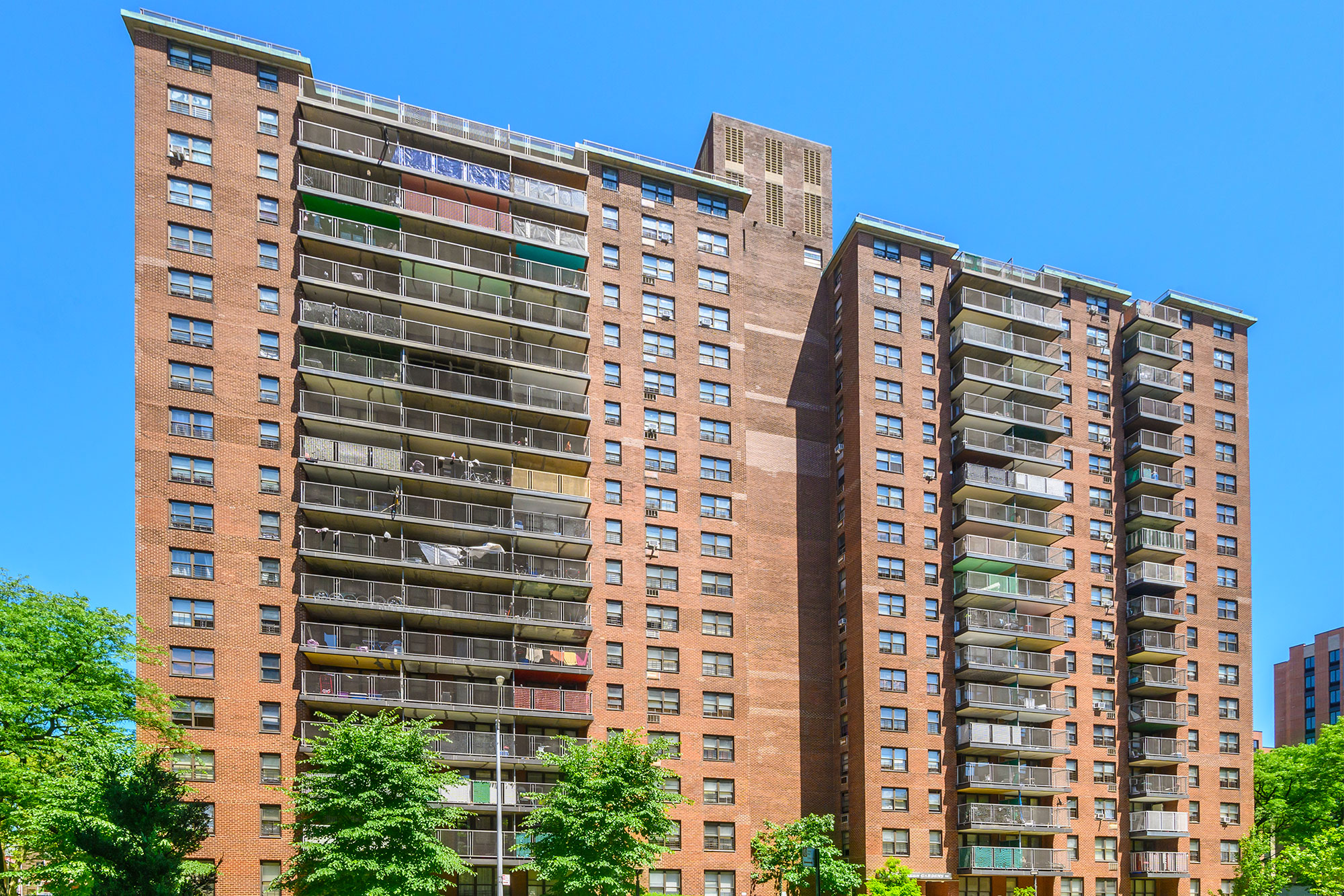 Looking up at the large brick building called Evergreen Gardens in Bronx, New York on a sunny Summer day.