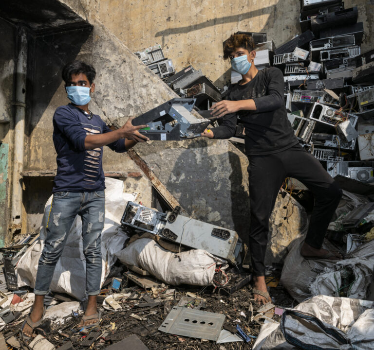 Men standing in a pile of e-waste