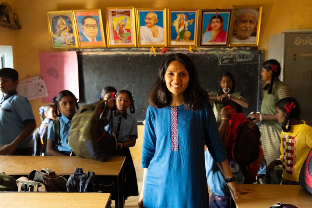 A female NGO worker standing in a classroom with students in the background