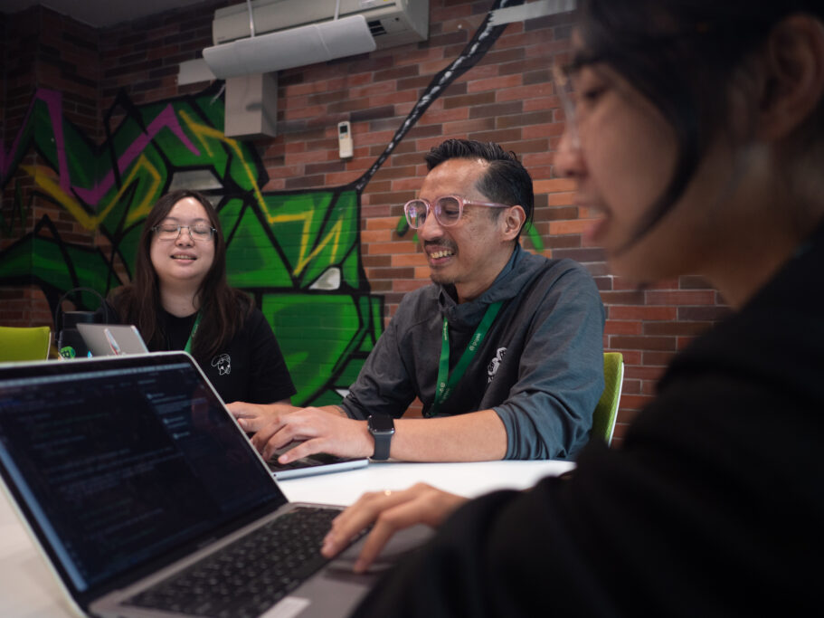 Two female software engineer and one male software engineers smiling working on their laptop