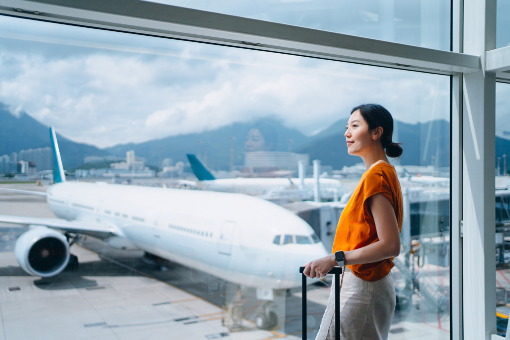 A woman stands in the airport holding onto a suitcase