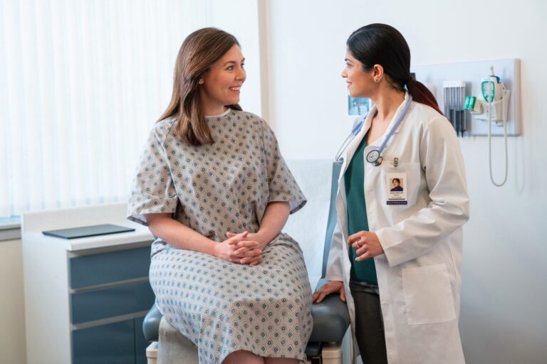 A medical clinician talking with a patient in an exam room.