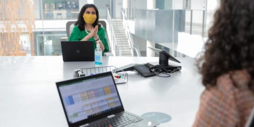 Two women practice social distancing in an office meeting