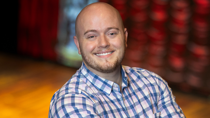 Smiling man stands near a stage in a theatre