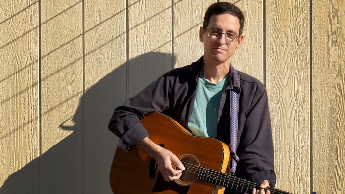 A smiling man holds a guitar