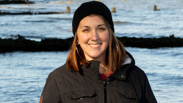 Smiling woman, clad in winter coat and hat, stands near water