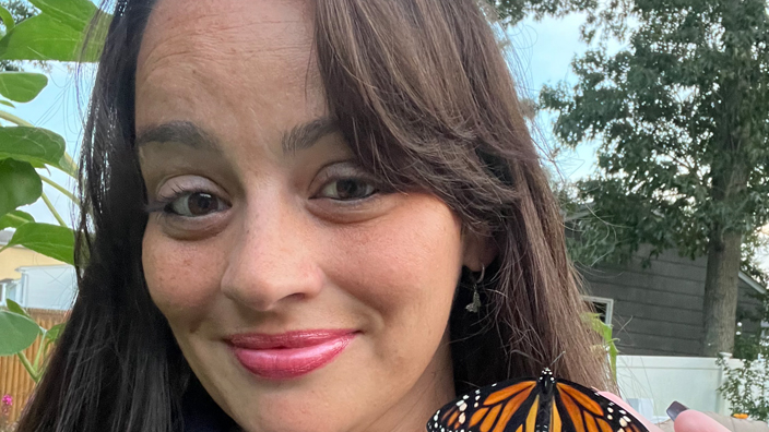 A smiling woman holds a butterfly in her hand