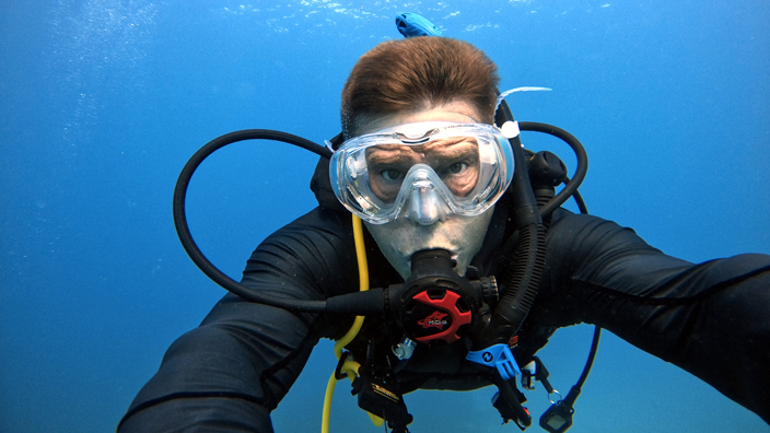 A man wearing scuba diving equipment floats under water