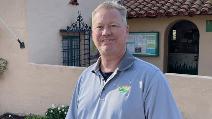 A man wearing a light blue shirt stands in front of a building