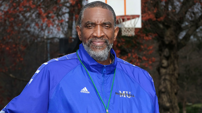 A man in a blue athletic suit holds a basketball