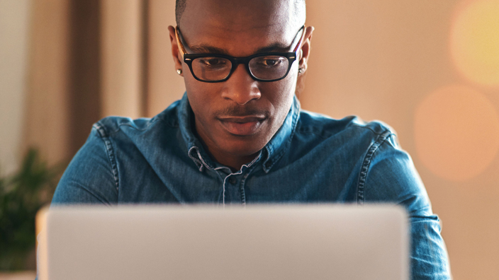 A man wearing glasses works on a laptop computer.