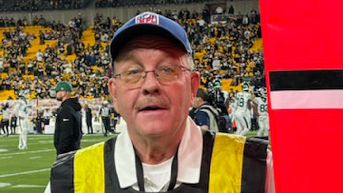 A man wearing a yellow and black vertically striped vest stands on the sideline of a football field.