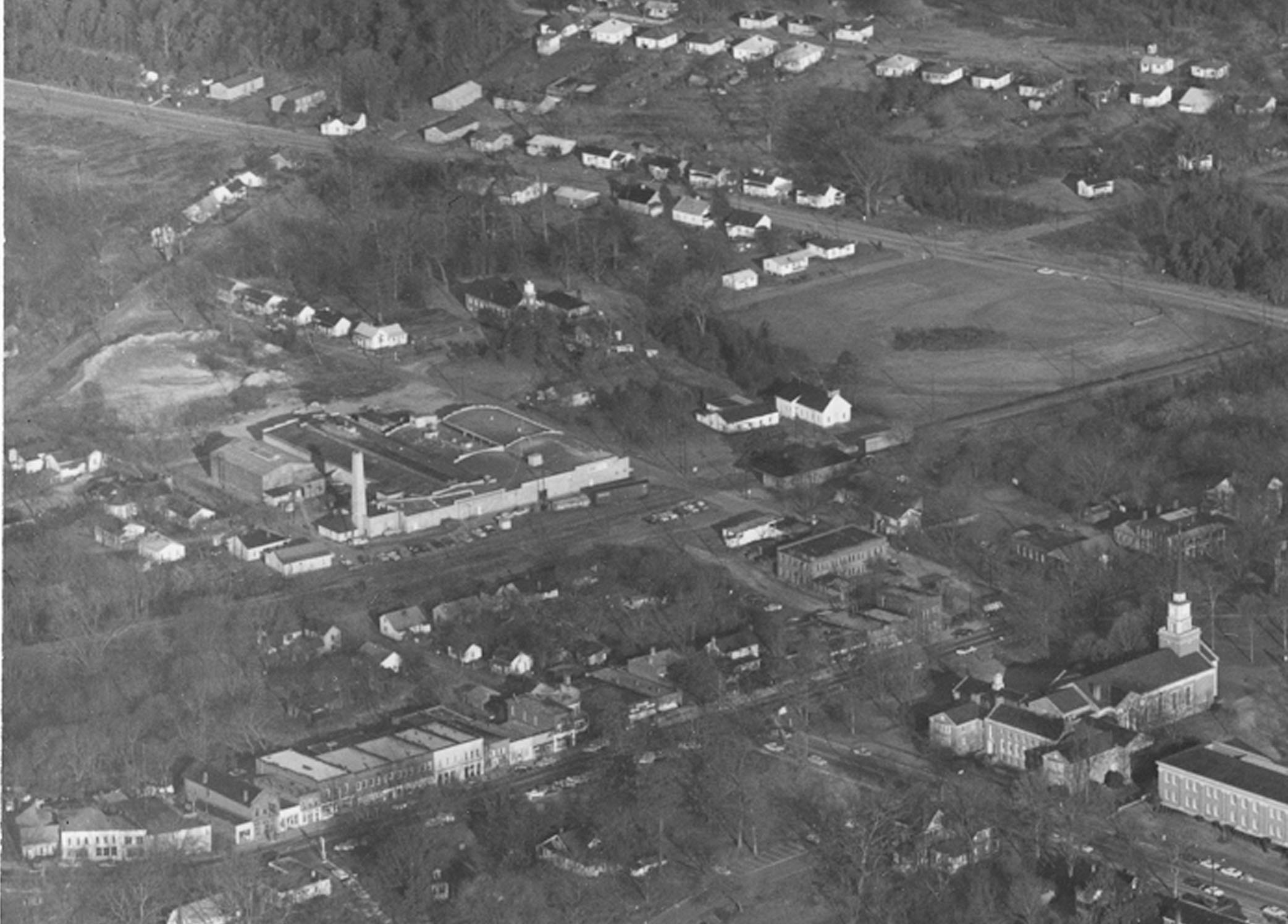 Aerial photo of the Linden Mill, later the Carolina Asbestos Co., with smokestack, in downtown Davidson. Main Street and Davidson College Presbyterian Church are at the bottom. Probably from the 1950s or 1960s. (Davidson College Archives)