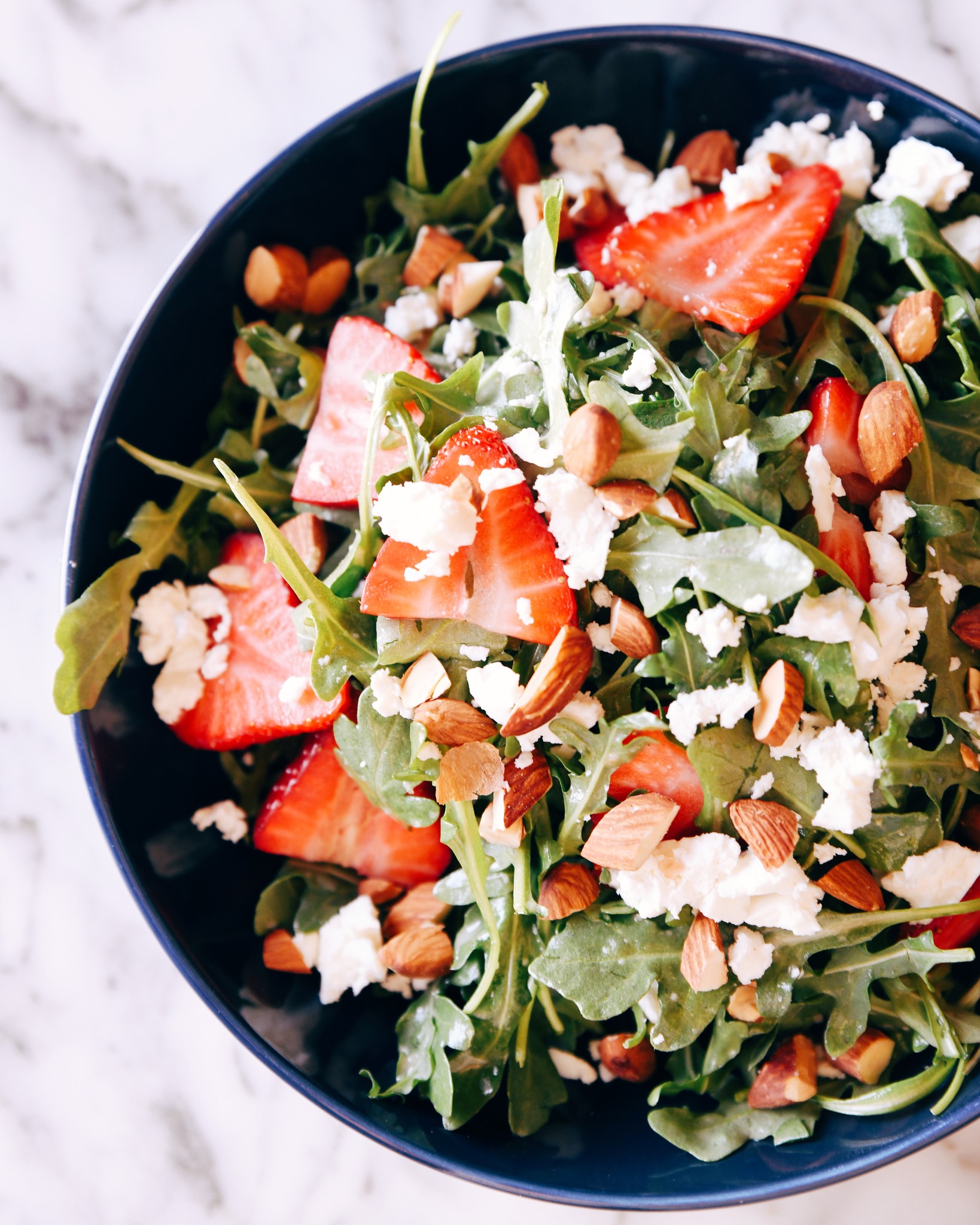 An arugula salad with strawberries, almonds and cheese.