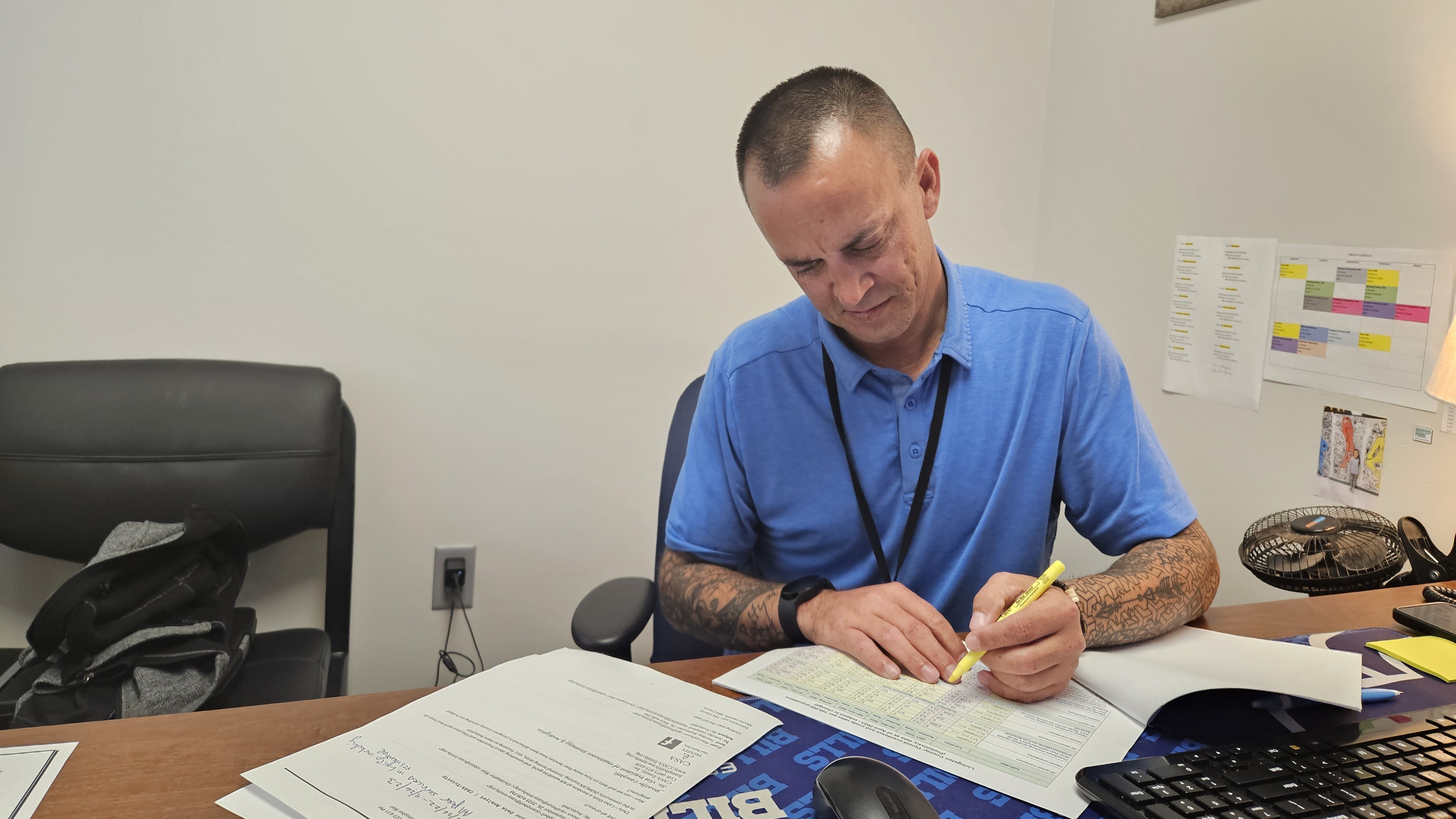 Recovery specialist Chris Blair, a white man in a blue polo sitting at a desk, highlights drug overdose statistics for Livingston County in Western New York.