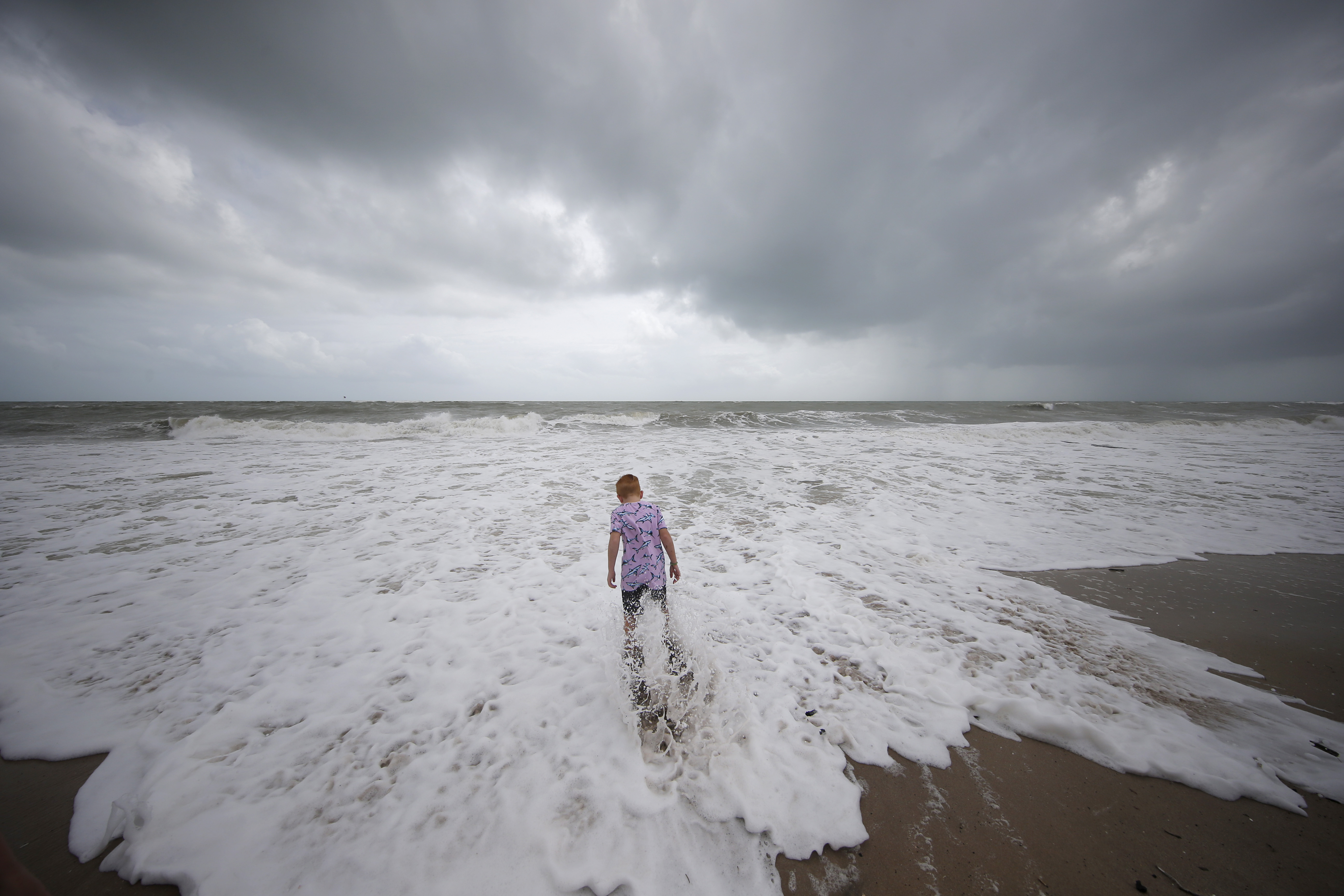 A boy stands near the high surf from the Atlantic Ocean