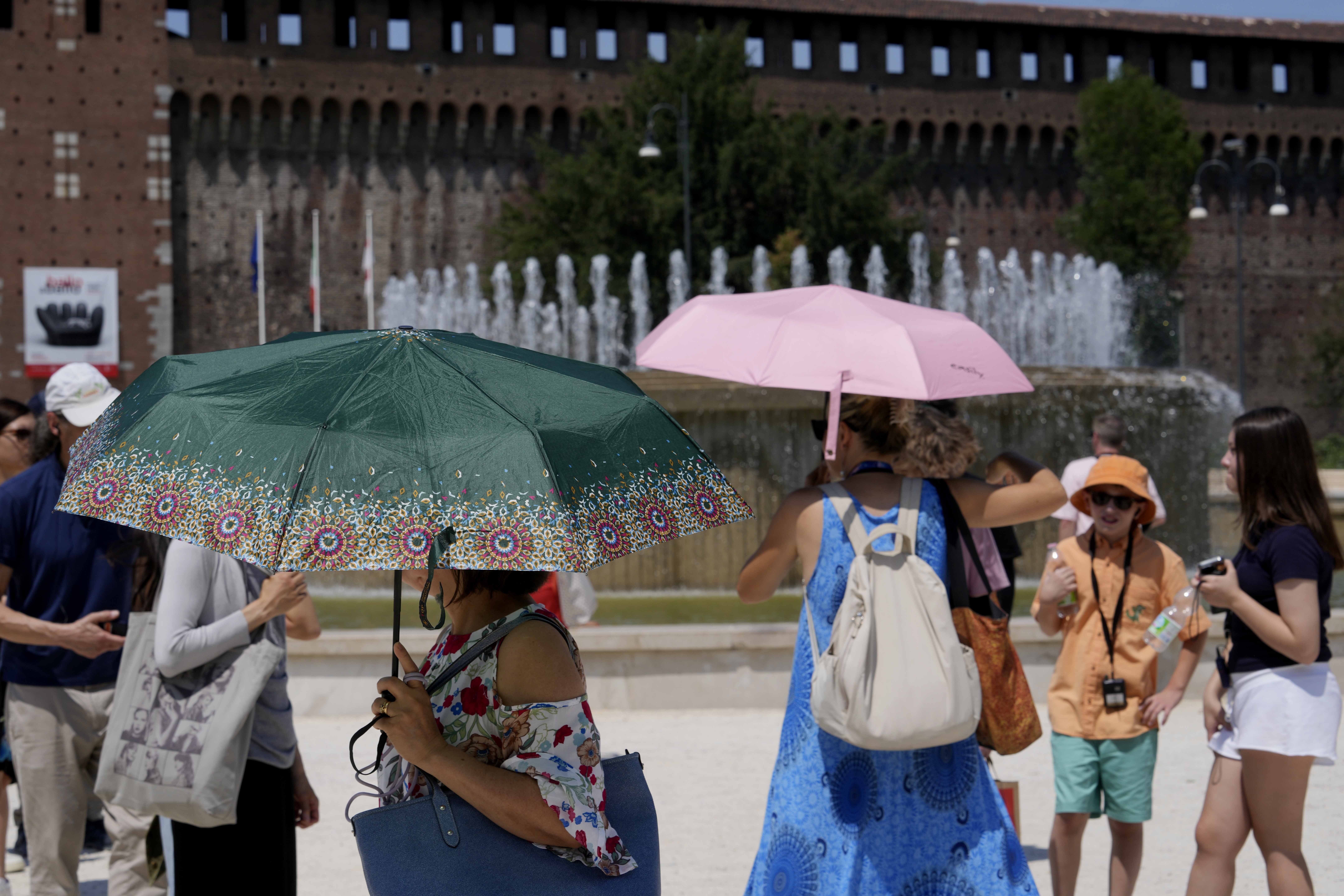 Tourists shelter from the sun in front of the Sforzesco Castle in Milan, Italy, on Tuesday. Weather alerts, forest fires, melting pavement in cities: A sizzling heat wave has sent temperatures in parts of central and southern Europe soaring toward 104 degrees Fahrenheit (40 degrees Celsius) in some places.