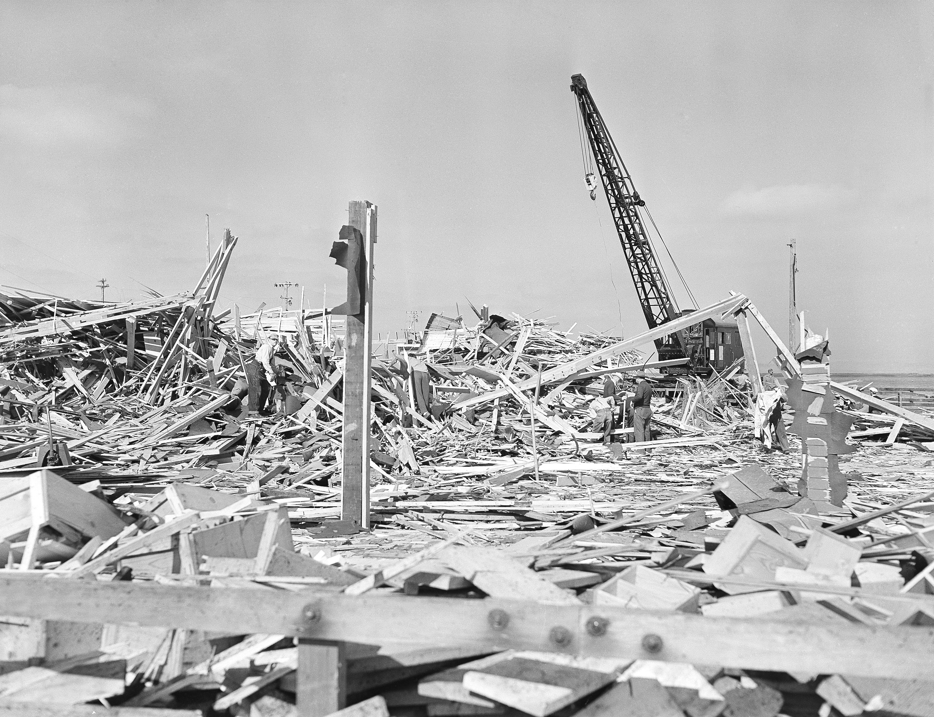 Workmen searched through the debris of what was the carpenter shop on the pier at Port  in Chicago, Calif. on July 18, 1944 after the building was leveled by the explosion of two munition ships the evening of July 17. Other buildings on the waterfront and in the town itself were shattered by the terrific blast, which was felt 50 miles from the scene. 