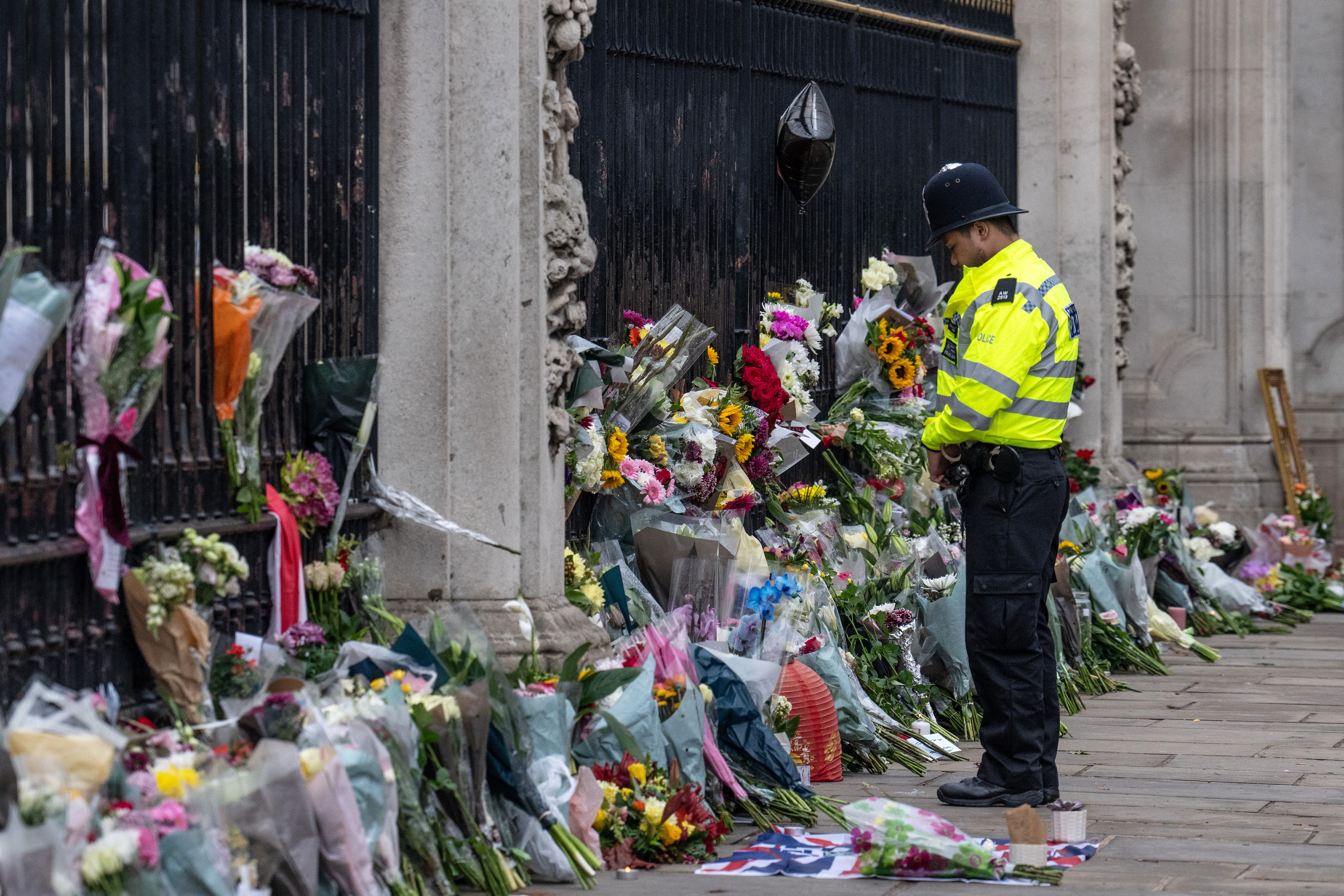 A guard looks down at bouquets of flowers piled outside the gates of Buckingham Palace. 