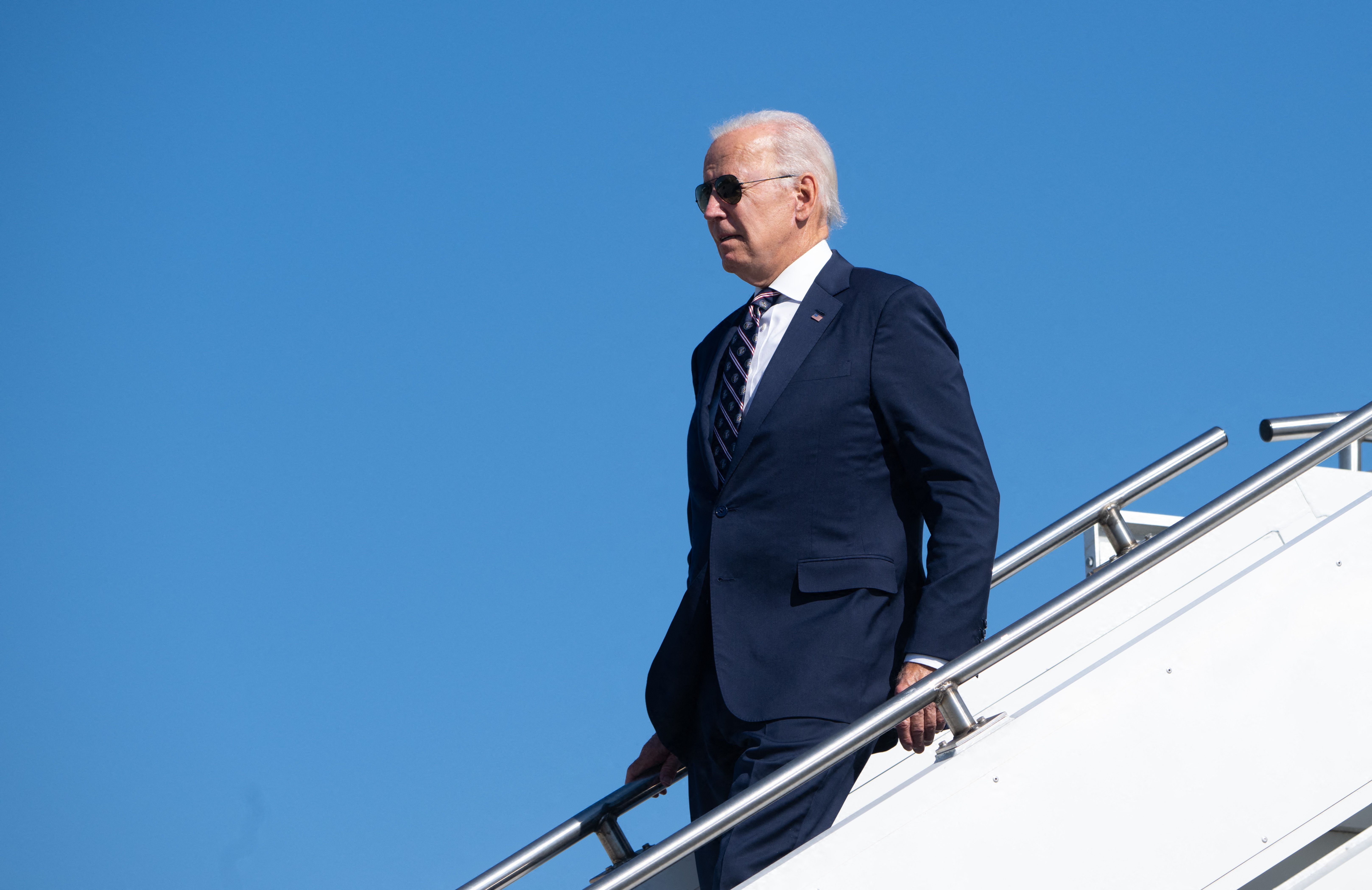 President Biden walks down the steps of Air Force One against a blue sky.
