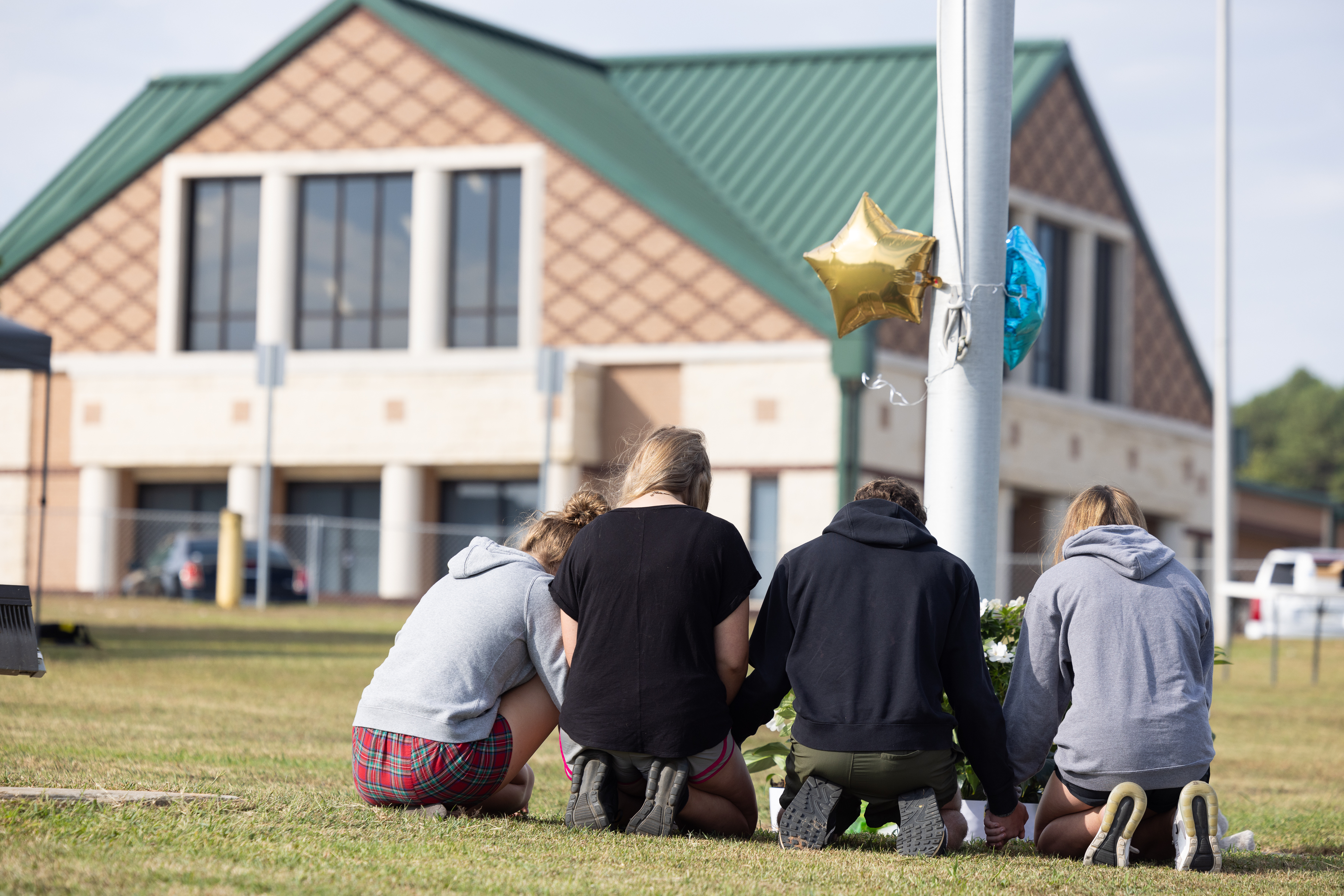 Students kneel in front of a makeshift memorial in front of Apalachee High School on in Winder, Ga., on Thursday, one day after two students and two teachers were shot and killed at the school.