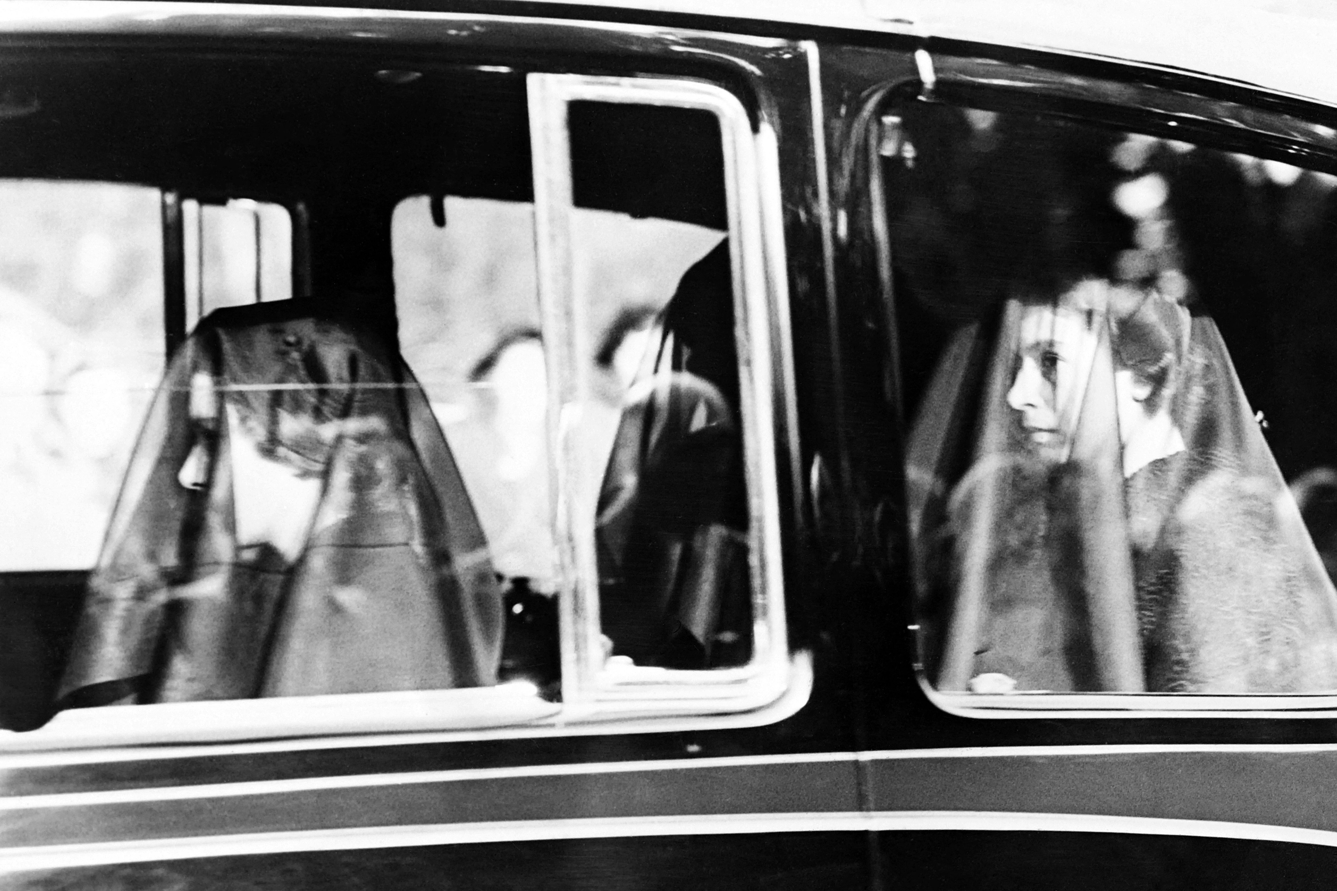 A black and white photo of three women wearing veils inside of a car. 