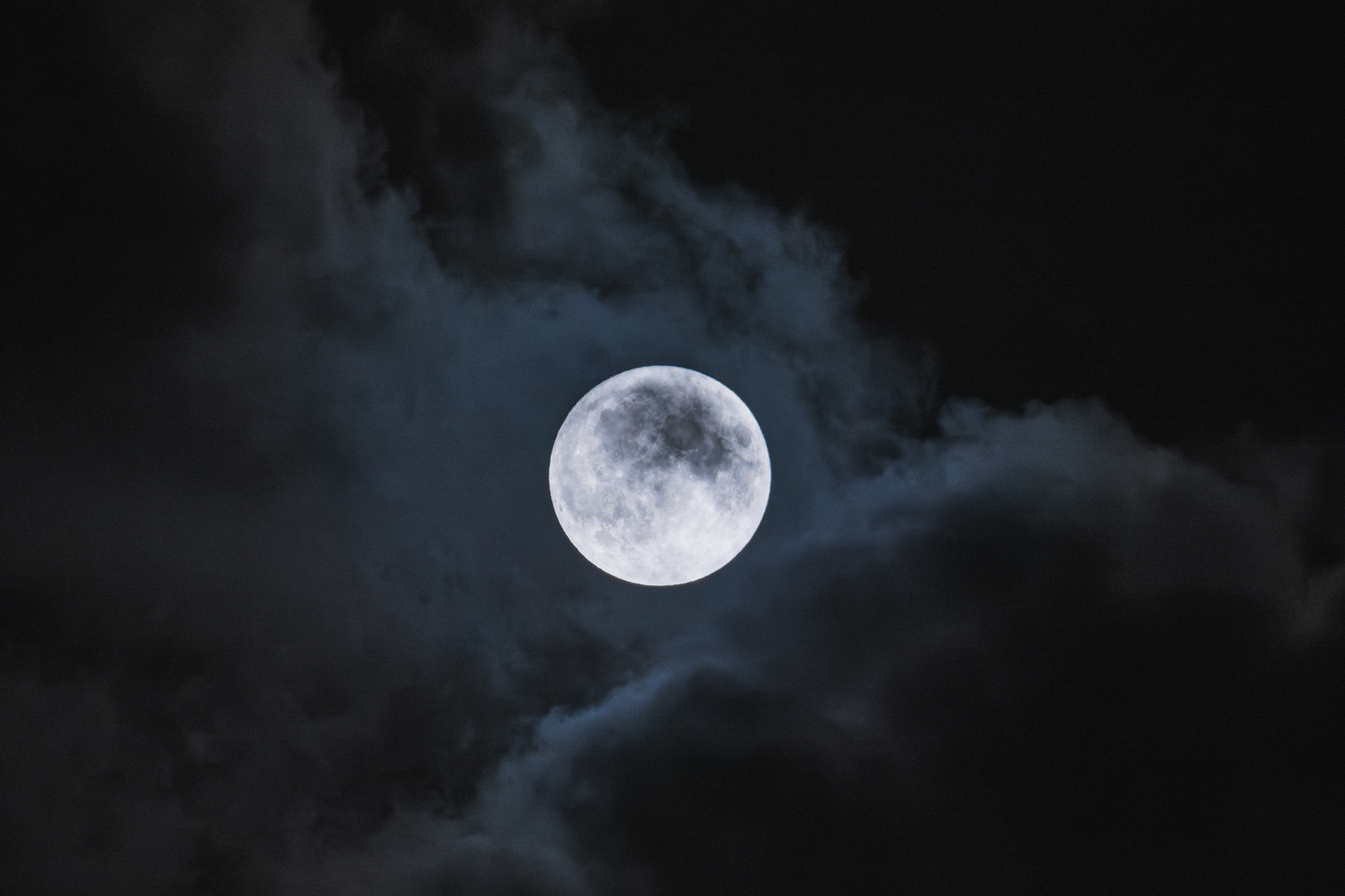 Amazing scenery of white glowing moon with craters in black sky with clouds at night