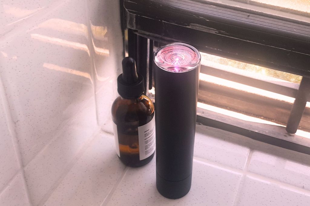 A lyma laser and a bottle of face oil in a bathroom setting.