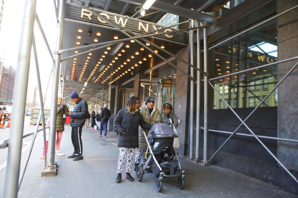 A group of people walking on the sidewalk outside The Row Hotel in Manhattan, marking the first day of NYC's 60-day maximum hotel stay limit for migrants.