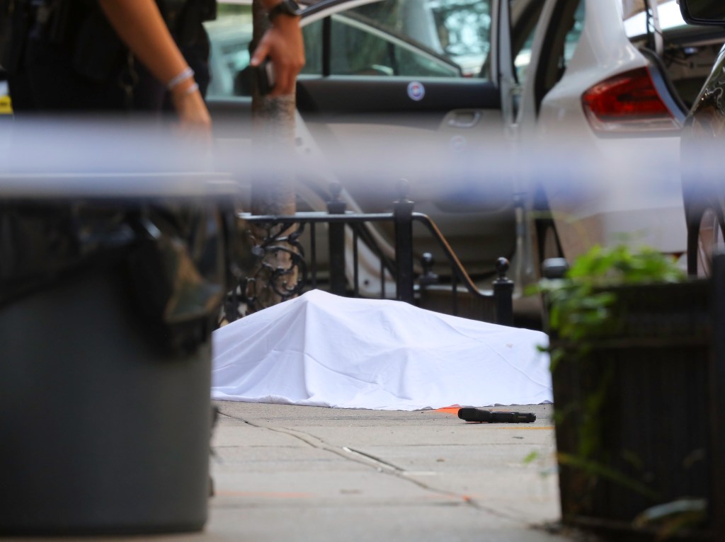 Body under white sheet with gun in foreground.