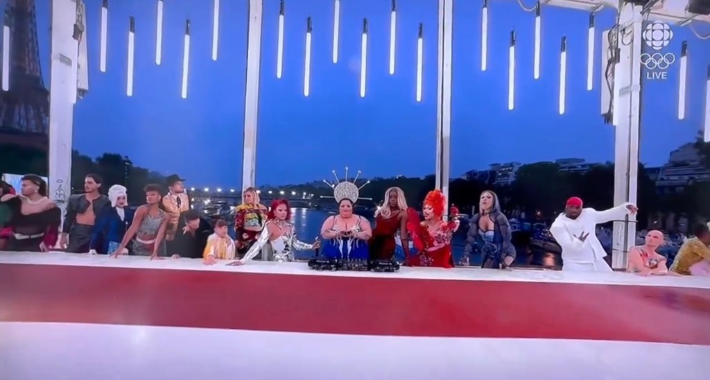 Drag queens stand behind the table.