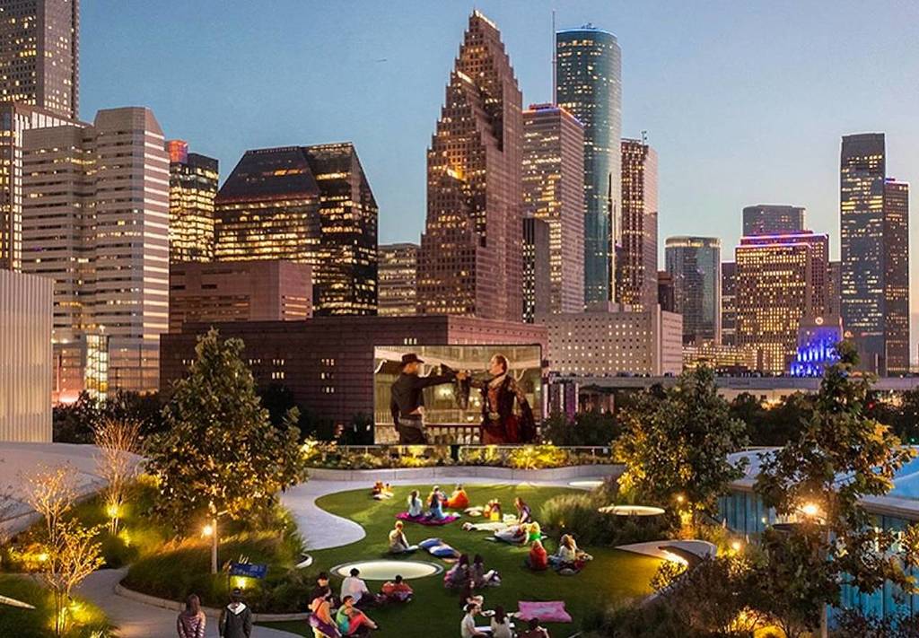 Rooftop lawn at Post with a visitors watching a movie, the downtown Houston skyline in the background.