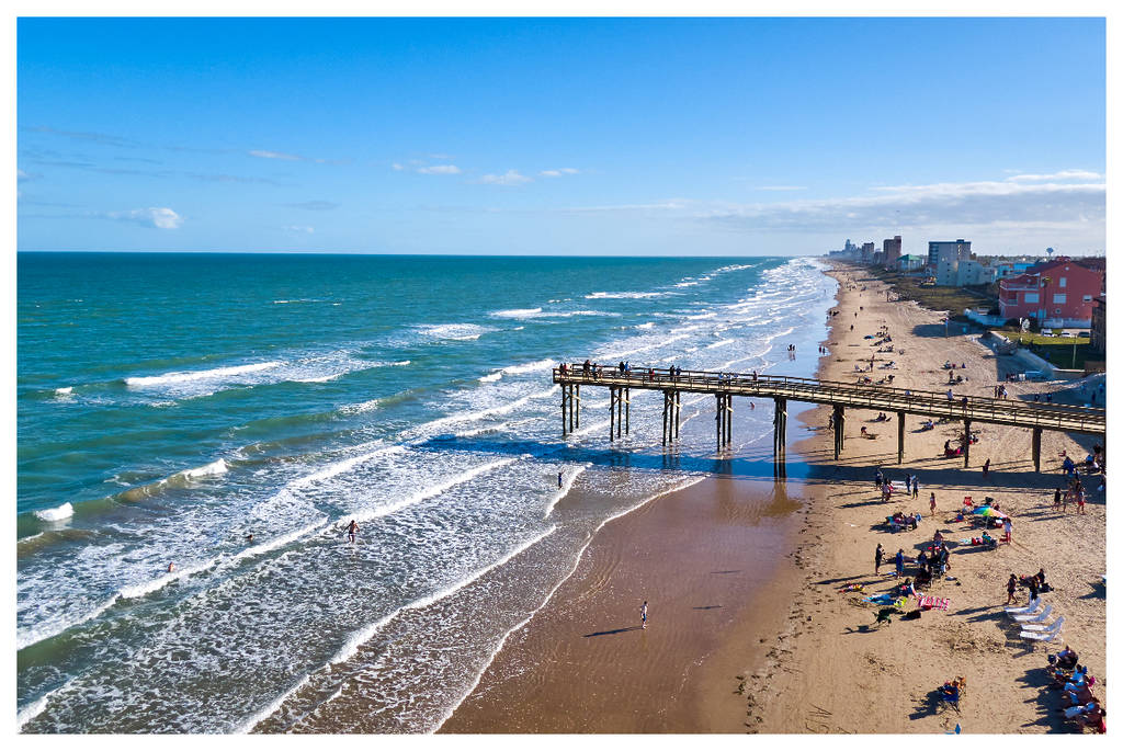 Aerial view of South Padre Island. Beach goers relax in the sun on the sand as waves lap the shoreline.