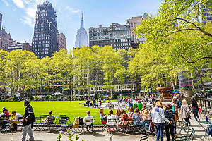 Springtime in Bryant park. People relaxing, green lawn and trees, clear blue sky and skyscrapers background