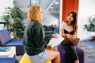 Two people talking, one person talks while holding documents and the other listens and holds a clipboard